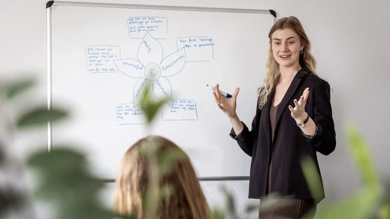 Kvinde underviser og forklarer foran tavle